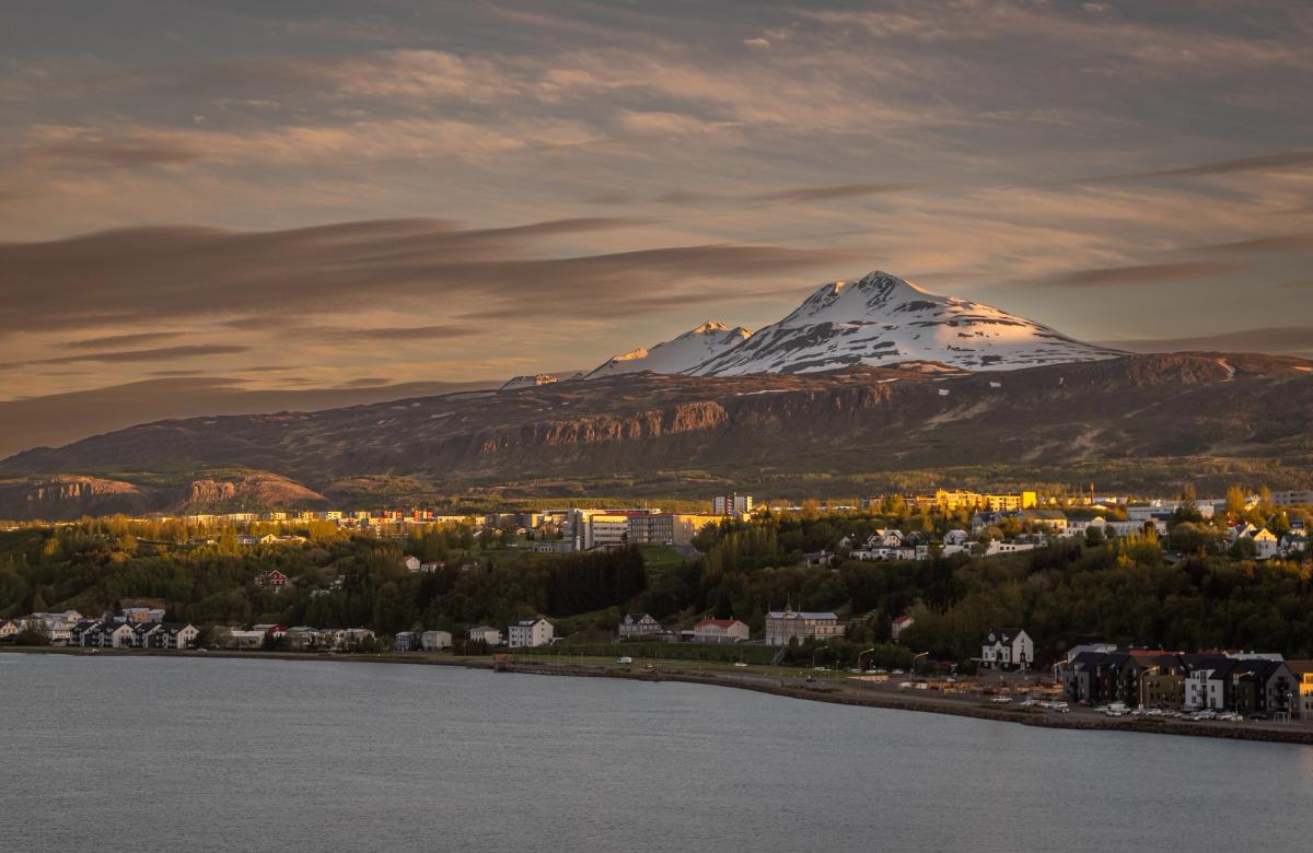A coastal town with a snow-capped mountain under a golden hour sky.