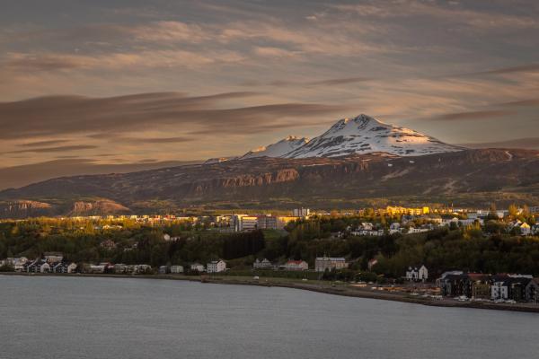 Pueblo costero junto a una bahía con una montaña nevada de fondo bajo un cielo nublado al atardecer.