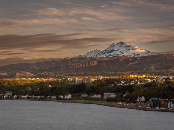 Snow-capped mountain overlooking a town along a bay at sunset.