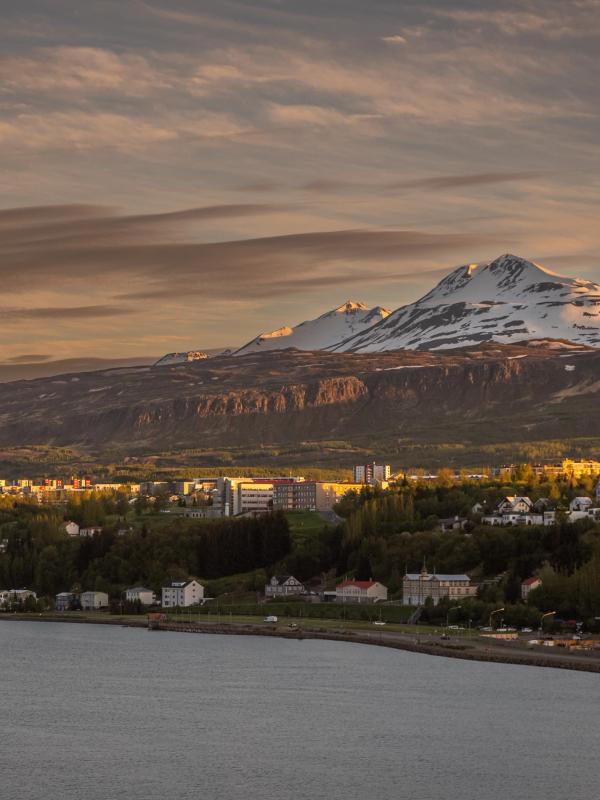 A coastal town with a snow-capped mountain under a golden hour sky.