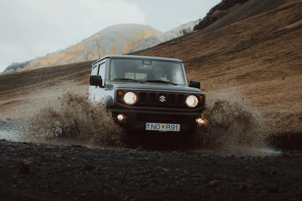 a suzuki suv is driving through a puddle on a dirt road