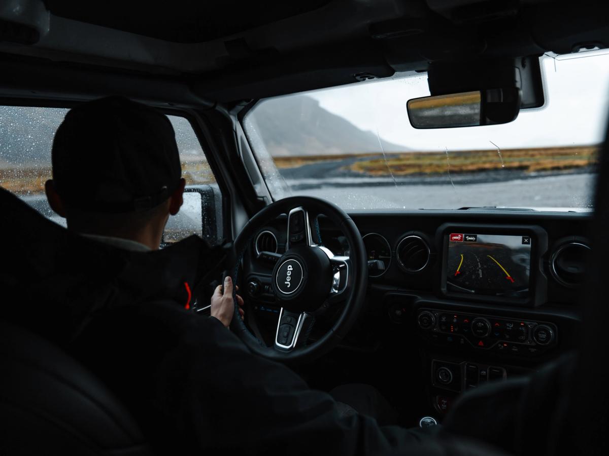 Ökumaður við stýrið Ökumaður undir stýri með snertiskjá í miðjunni og fjallveg fram undan