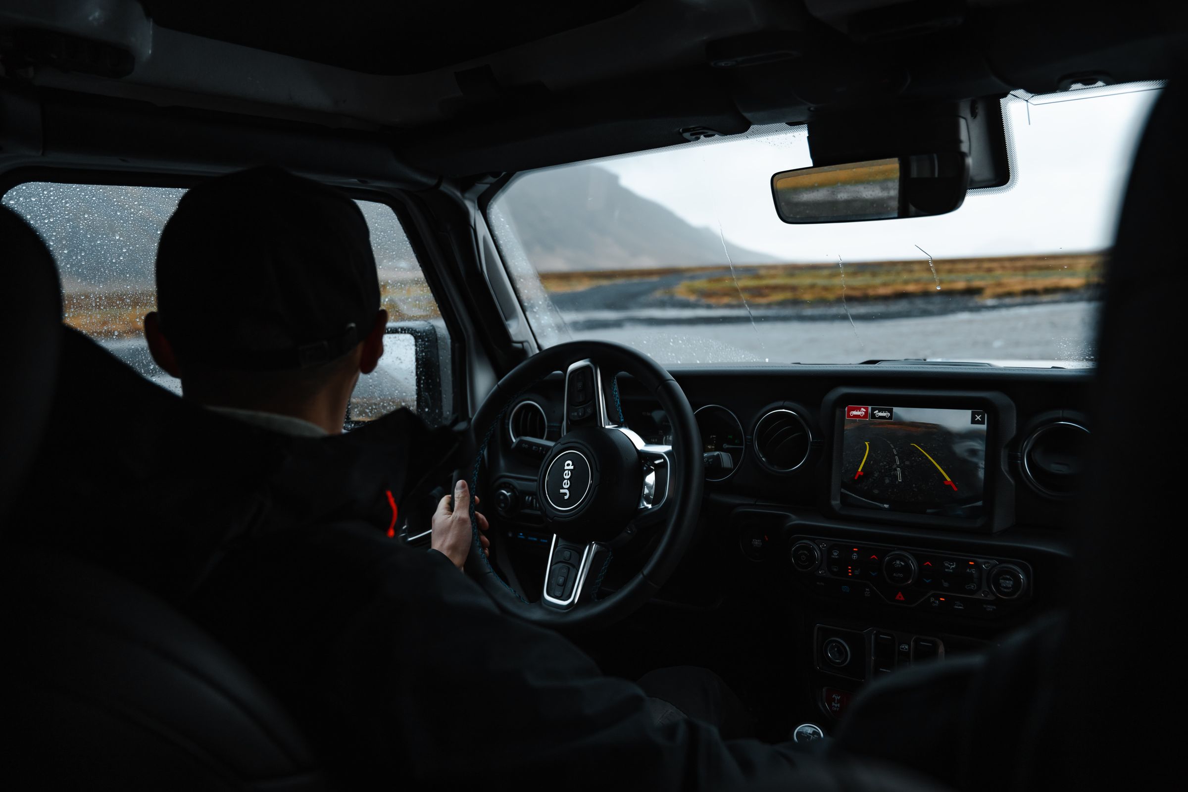 Ökumaður við stýrið Ökumaður undir stýri með snertiskjá í miðjunni og fjallveg fram undan
