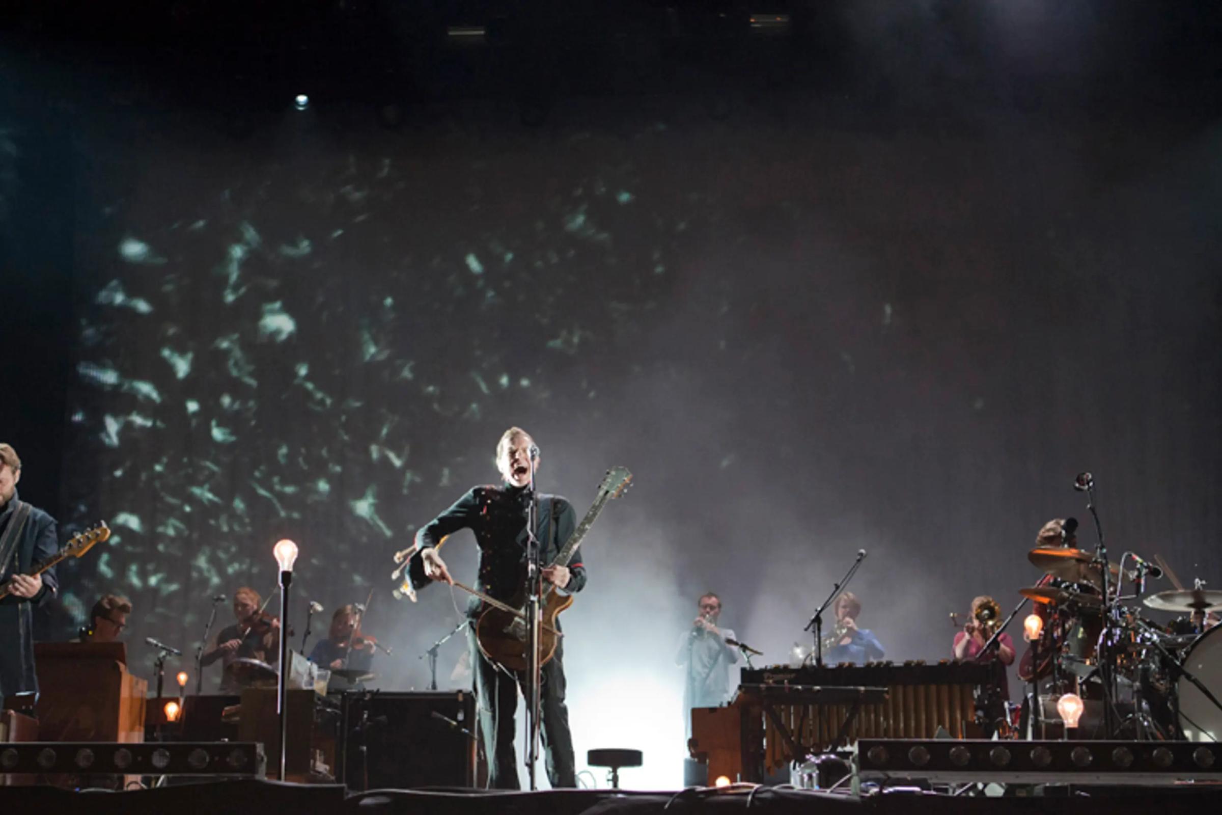 a man is playing a guitar on a stage with a band behind him .