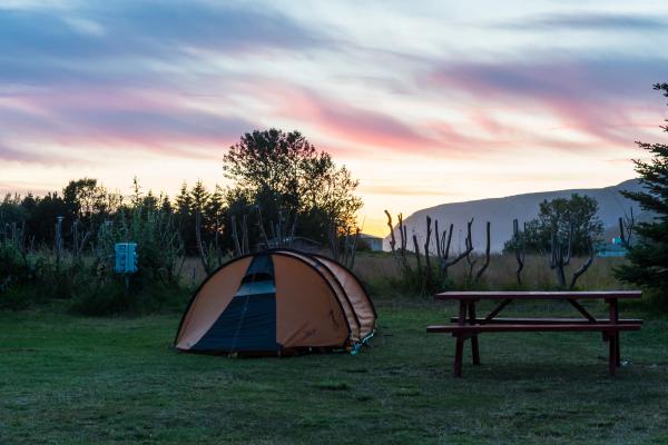 An orange camping tent and a red picnic table on a grassy field at sunset.