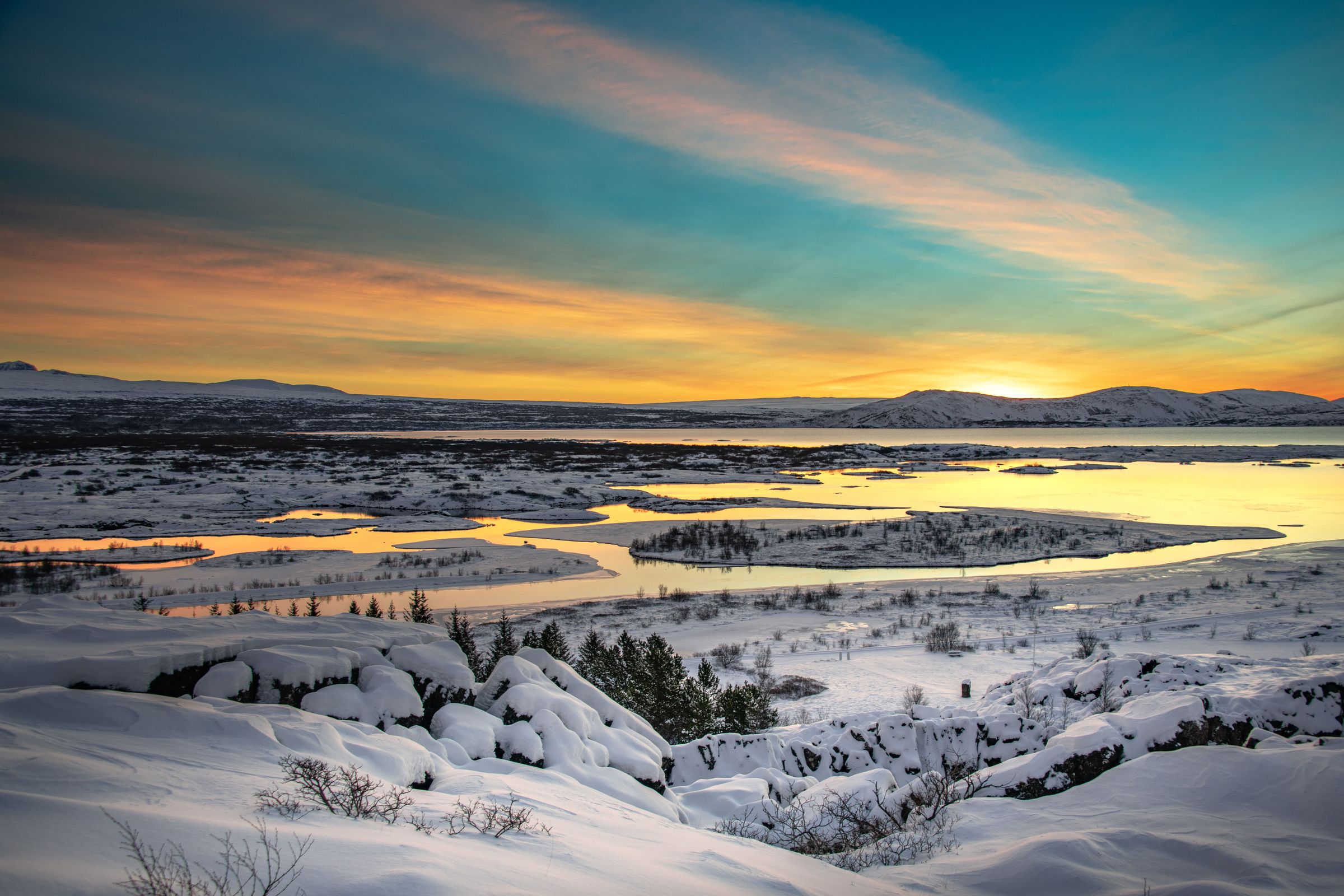 un paisaje nevado con un lago y montañas al fondo al atardecer.