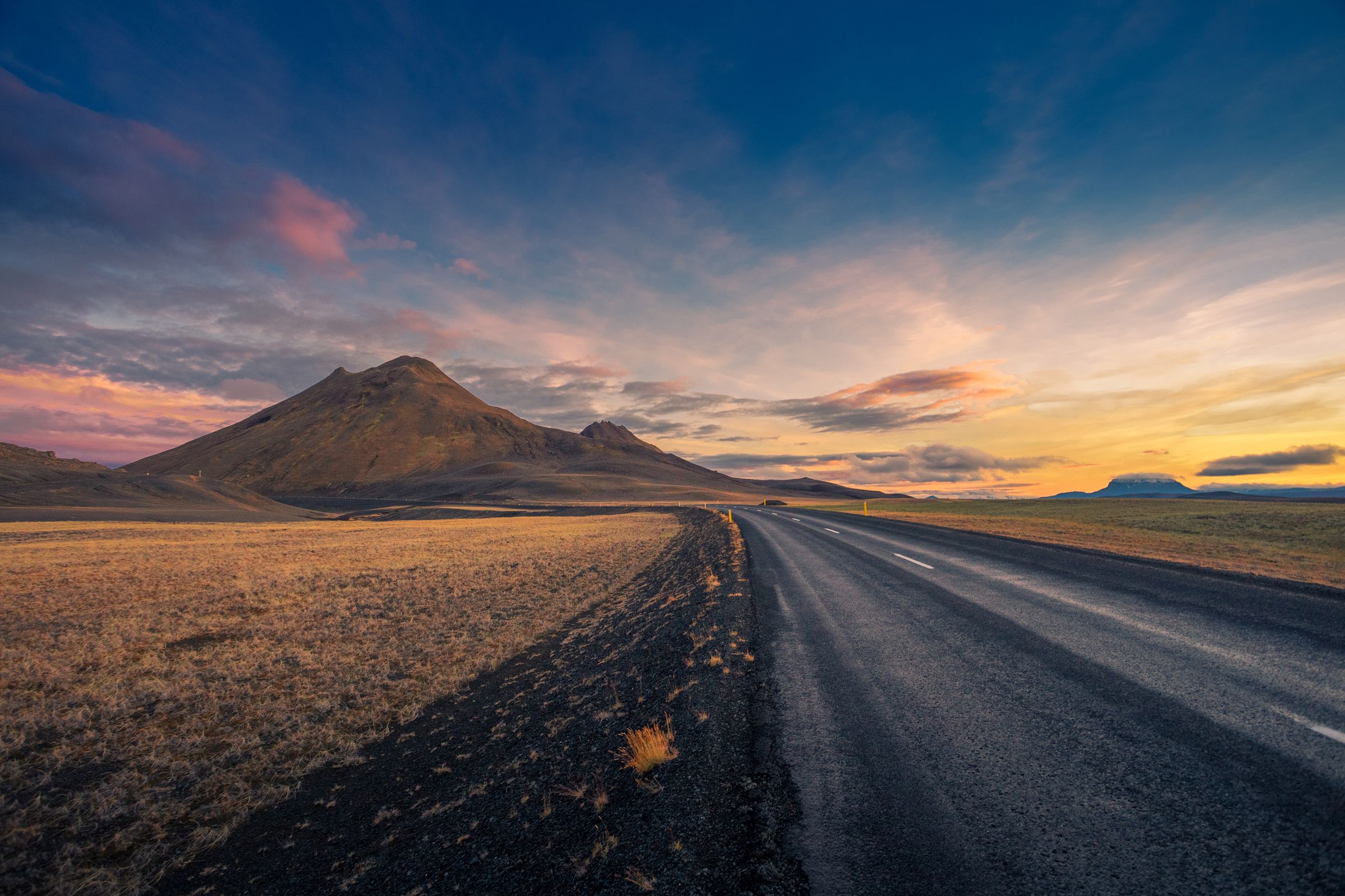 a road going through a desert with mountains in the background at sunset in iceland.