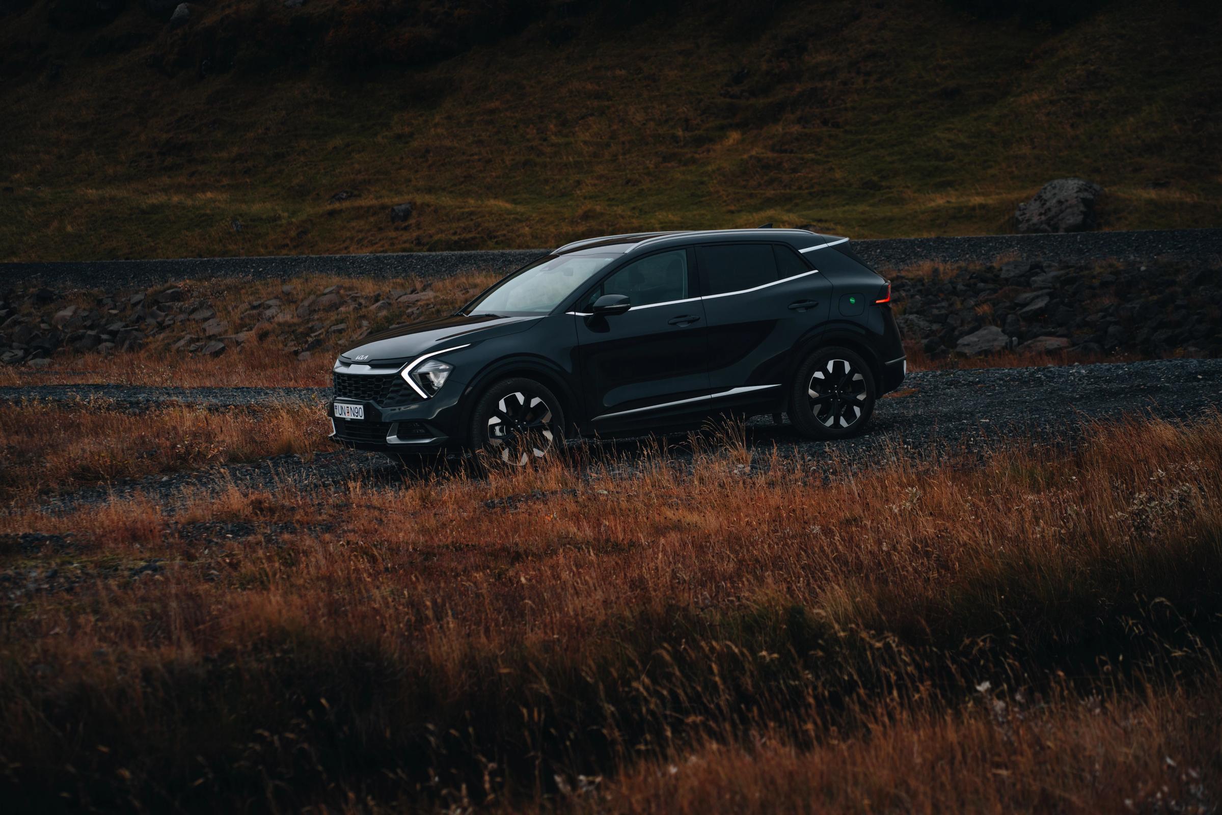 Kia Sportage séður skáhallt að framan, lagt á malarkanti við veginn við hliðina á háu grasi