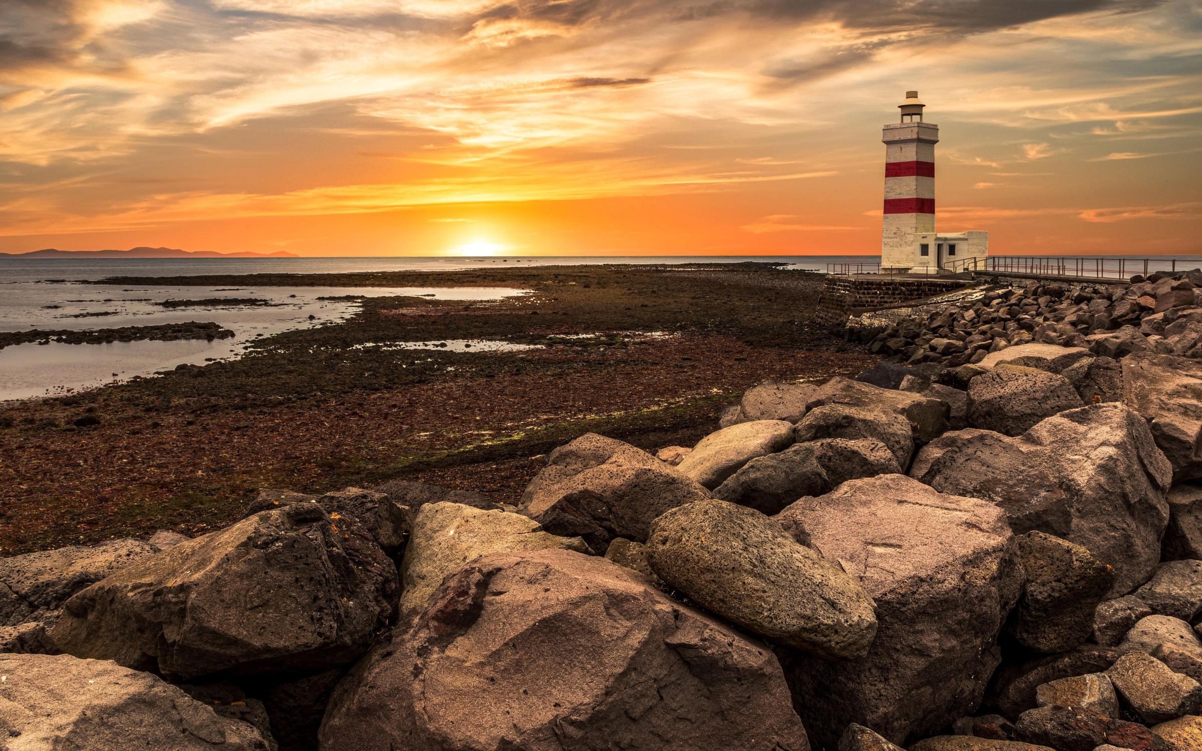 a lighthouse is sitting on top of a rocky beach at sunset .