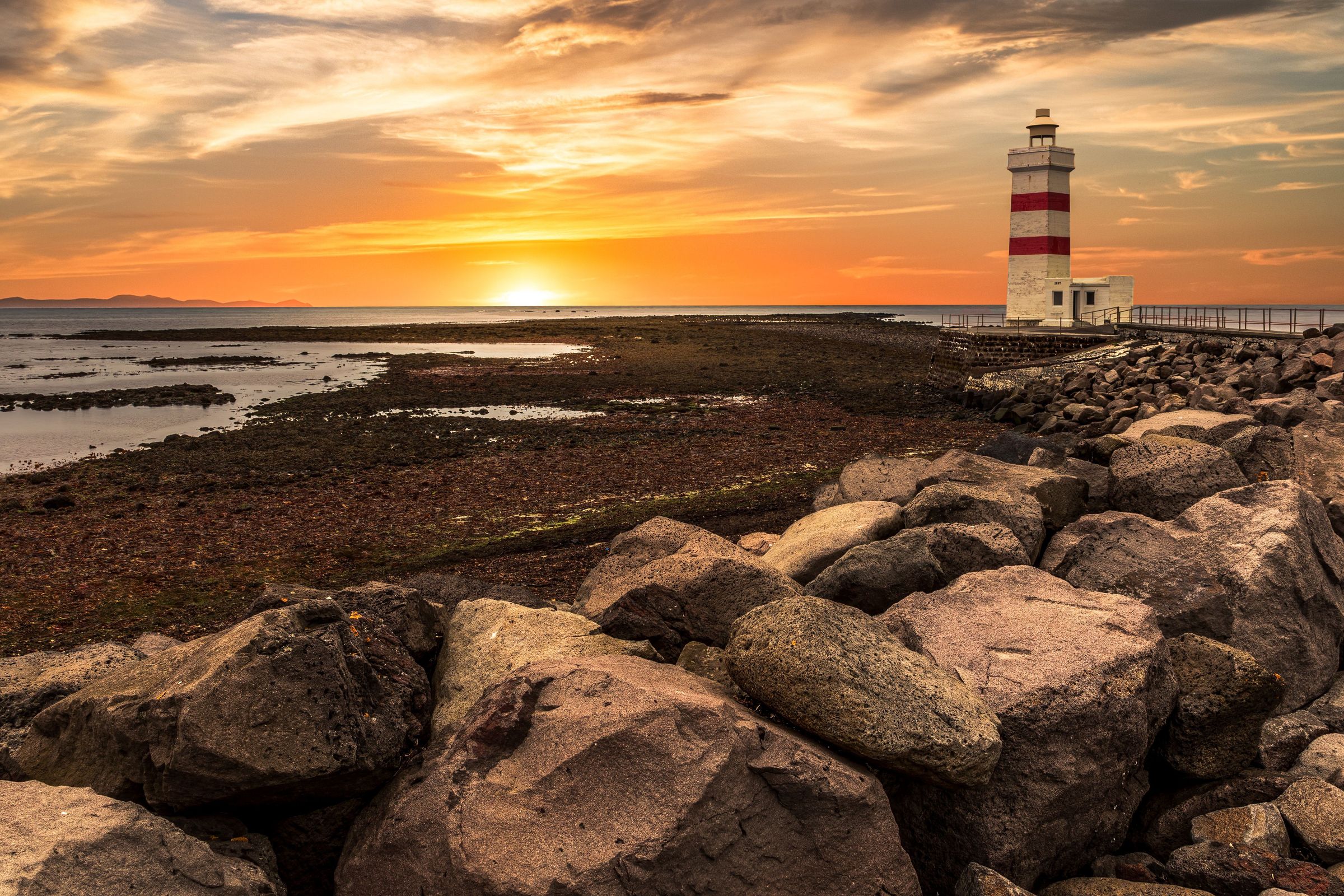 a lighthouse is sitting on top of a rocky beach at sunset .
