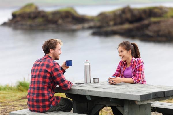 a man and a woman are sitting at a picnic table drinking coffee .