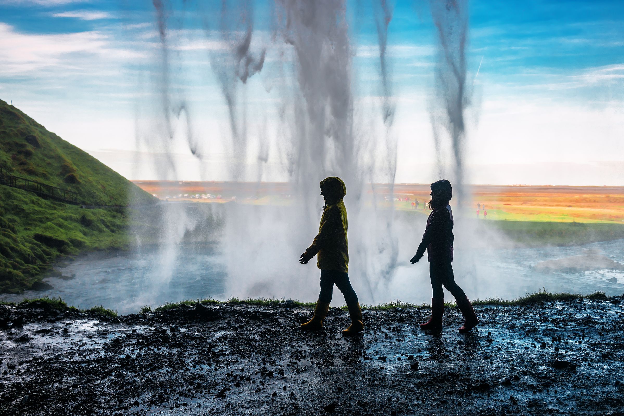 la silueta de dos personas caminando detrás de una cascada