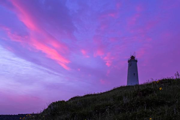 a lighthouse on top of a hill with a purple sky in the background .
