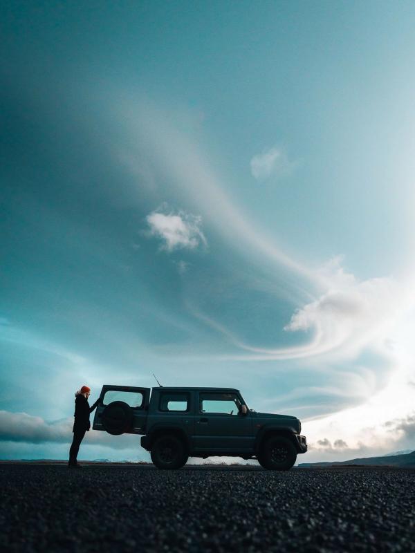 Iceland car rental A woman standing next to her rental car watching the Iceland landscape