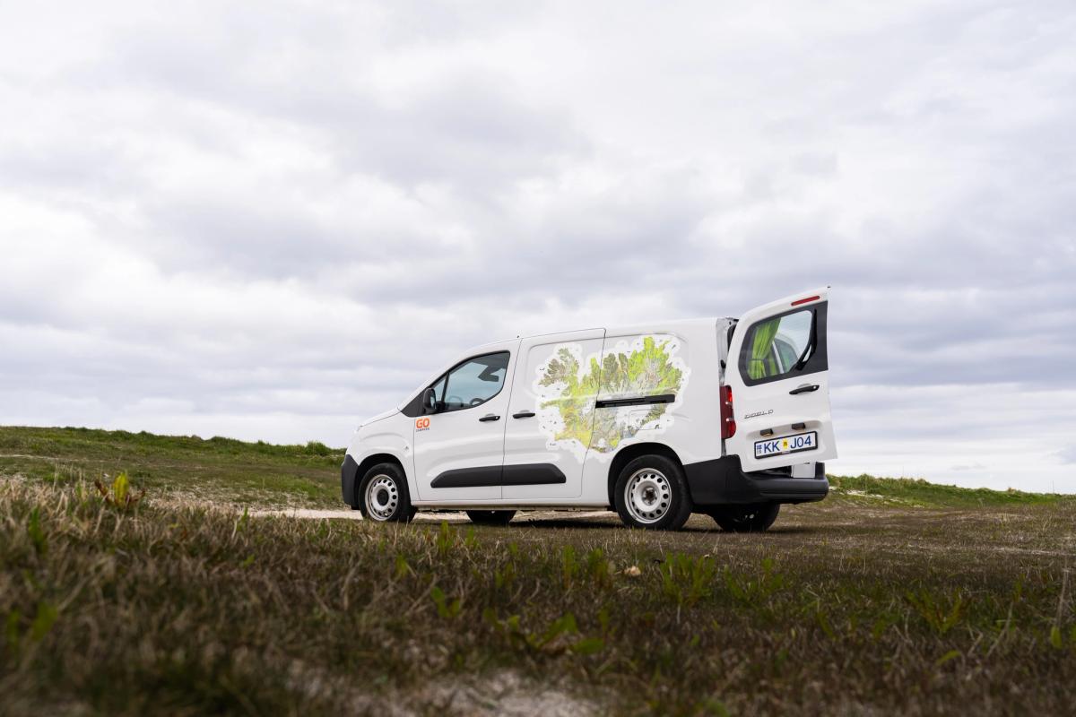 Vista lateral de una autocaravana compacta con la puerta trasera abierta en una pradera, alquiler de autocaravanas en Islandia