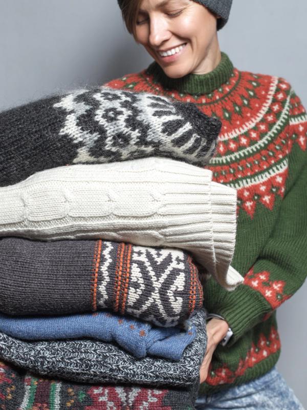 a woman is holding a pile of sweaters in her hands .