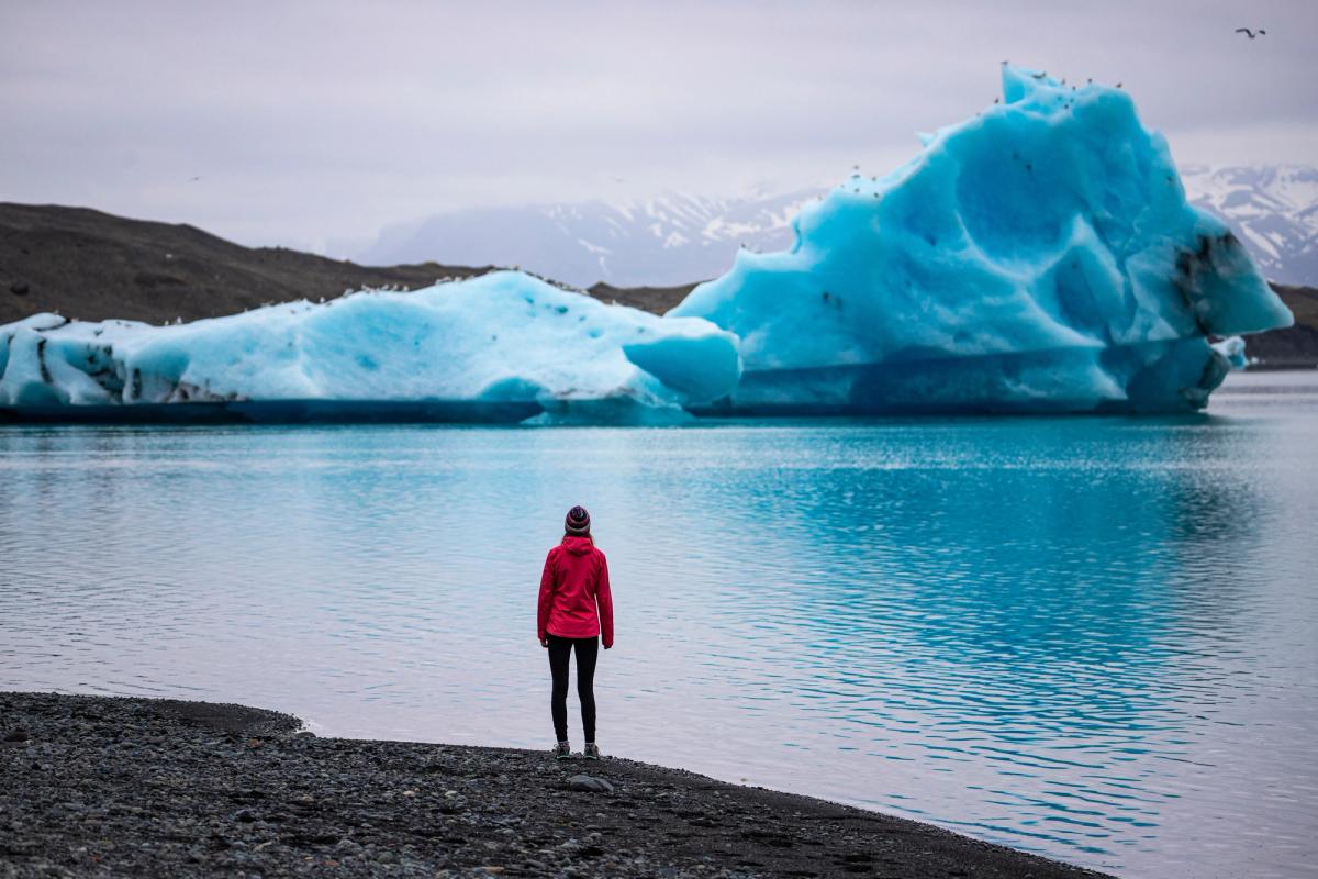 Mujer con una chaqueta roja en orilla de una laguna viendo un iceberg