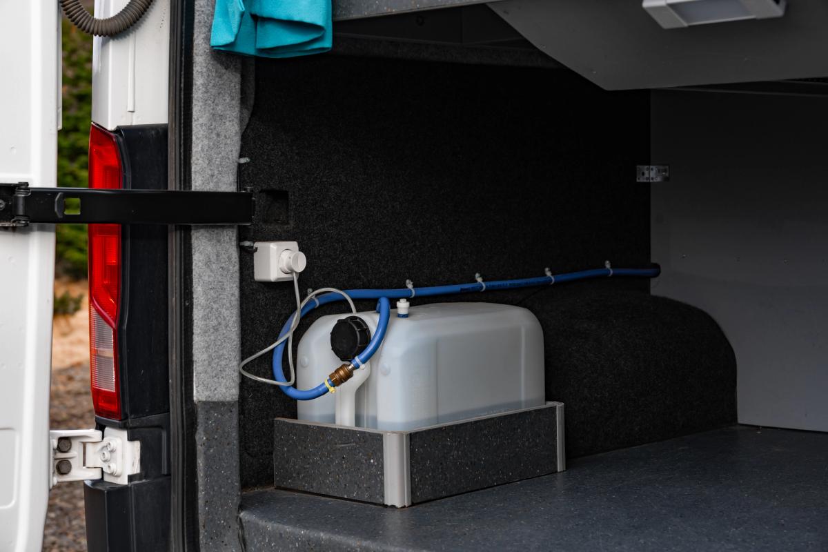Depósito de agua con una manguera azul de suministro y una toma de corriente en la zona de almacenamiento trasera