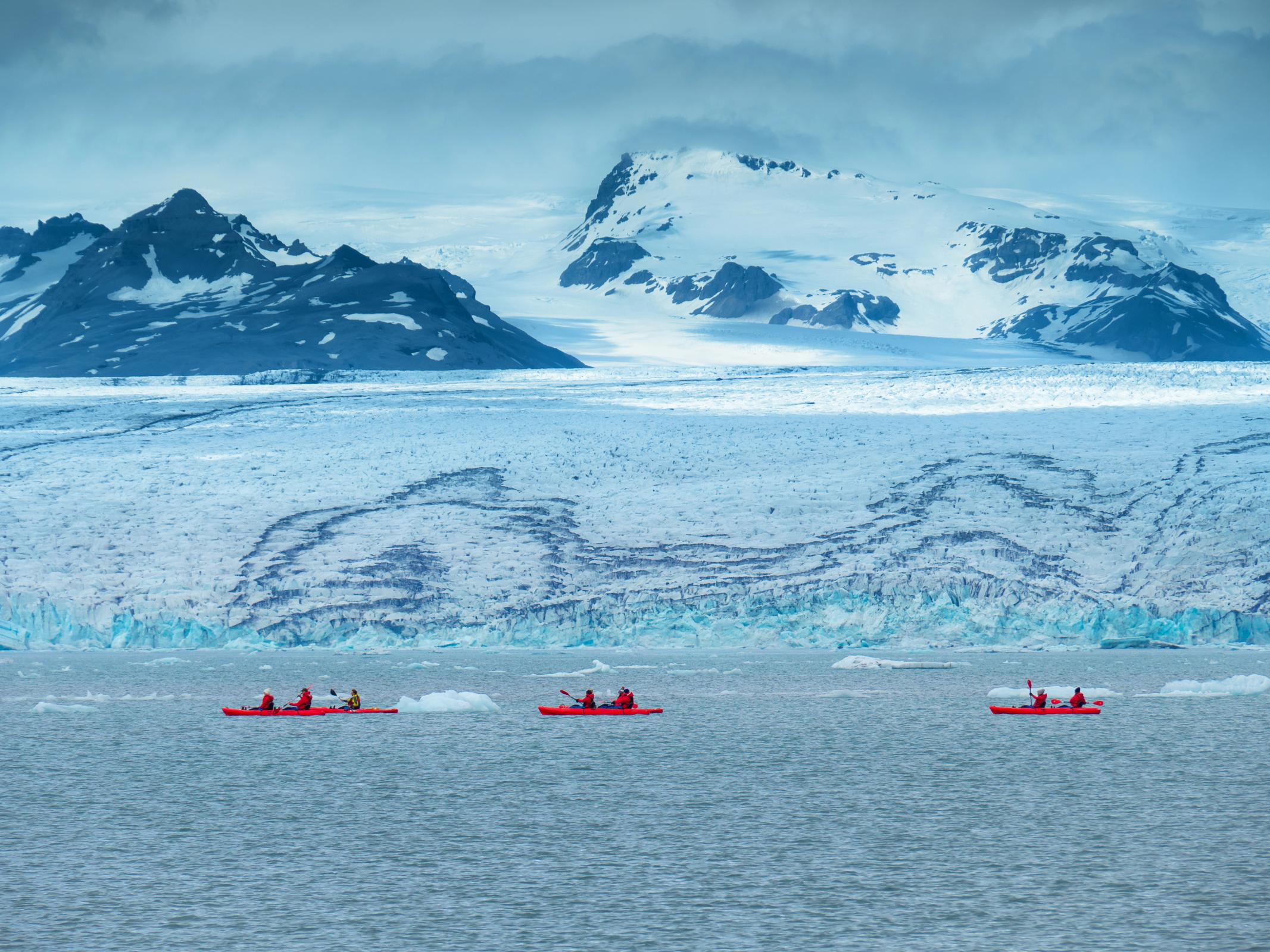 three kayaks next to a big glacier with mountains on the background