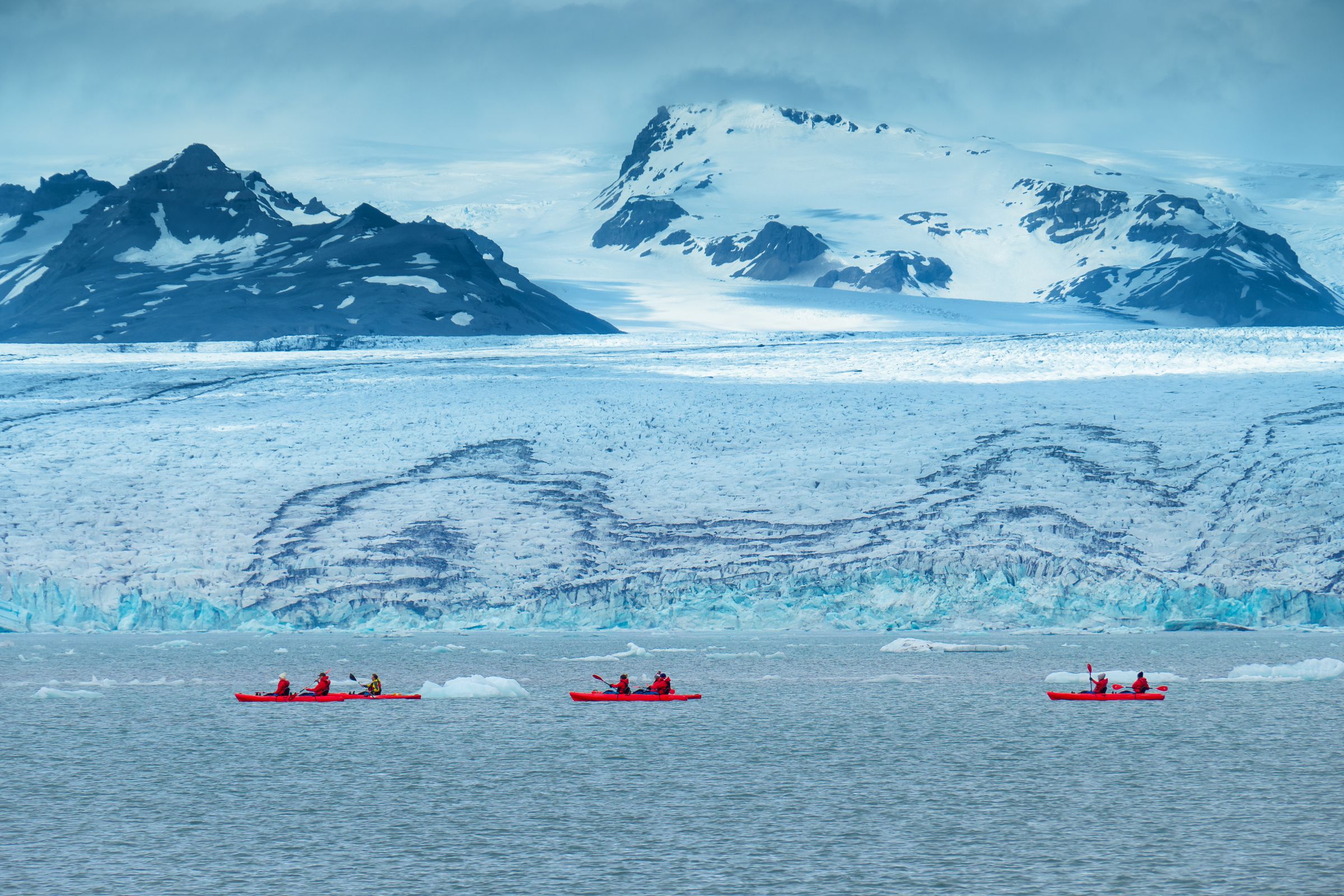 three kayaks next to a big glacier with mountains on the background