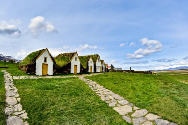 Tres casas de turba con caminos de piedra en un campo verde