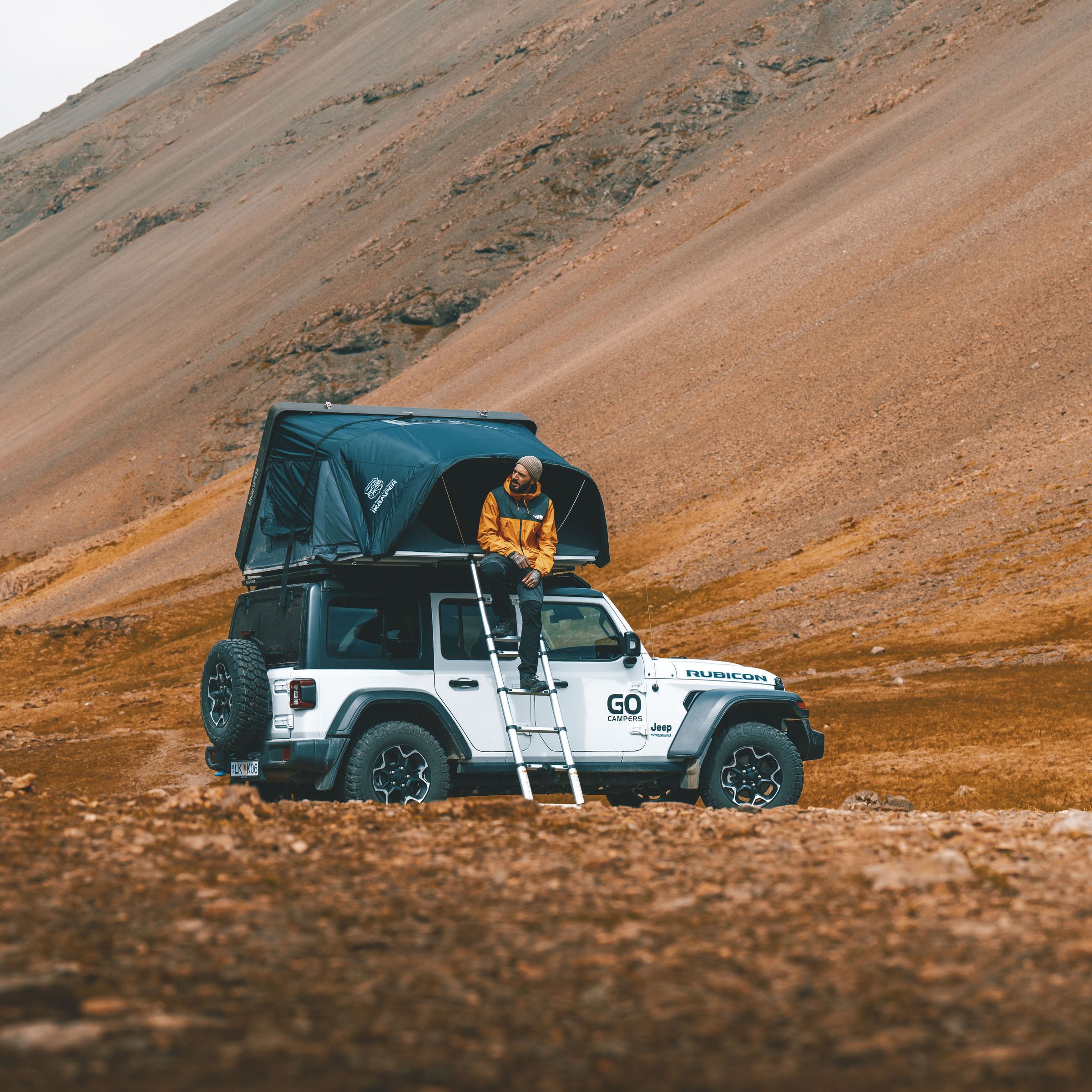 un hombre está sentado encima de un jeep con una tienda de campaña en lo alto.