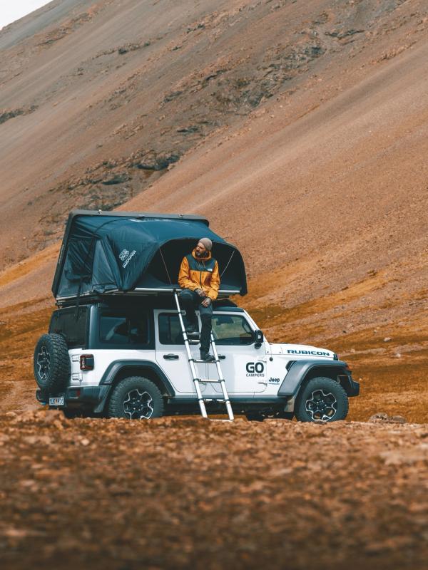 Un hombre sentado en el techo de un Jeep que tiene una tienda de campaña