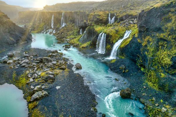 un paisaje con pequeñas cascadas que caen a un río muy azul sobre arena negra