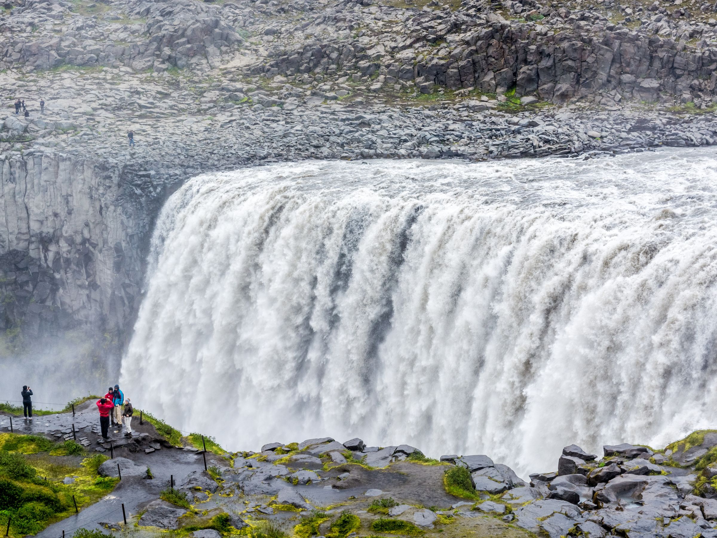 a group of people are standing on the edge of Dettifoss Waterfall
