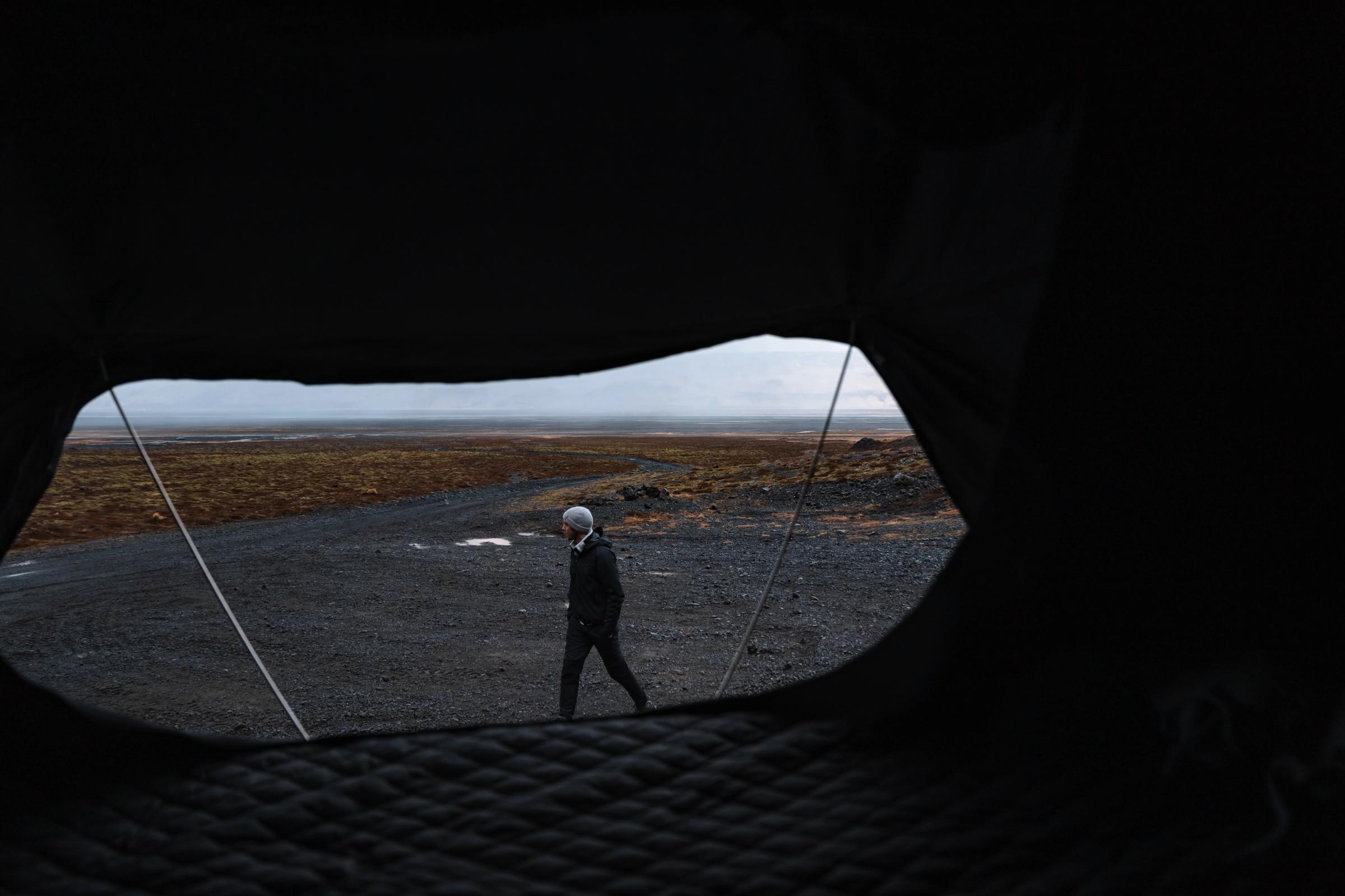 View from inside the rooftop tent of a person walking on an open gravel plain