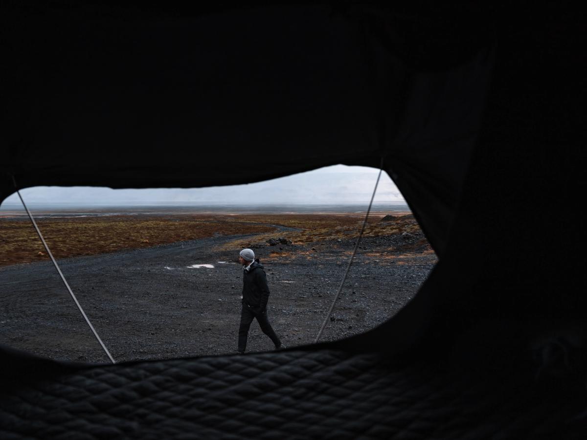 Útsýni yfir mölina úr tjaldi Útsýni innan úr þaktjaldi yfir manneskju sem gengur um opið malarsvæði