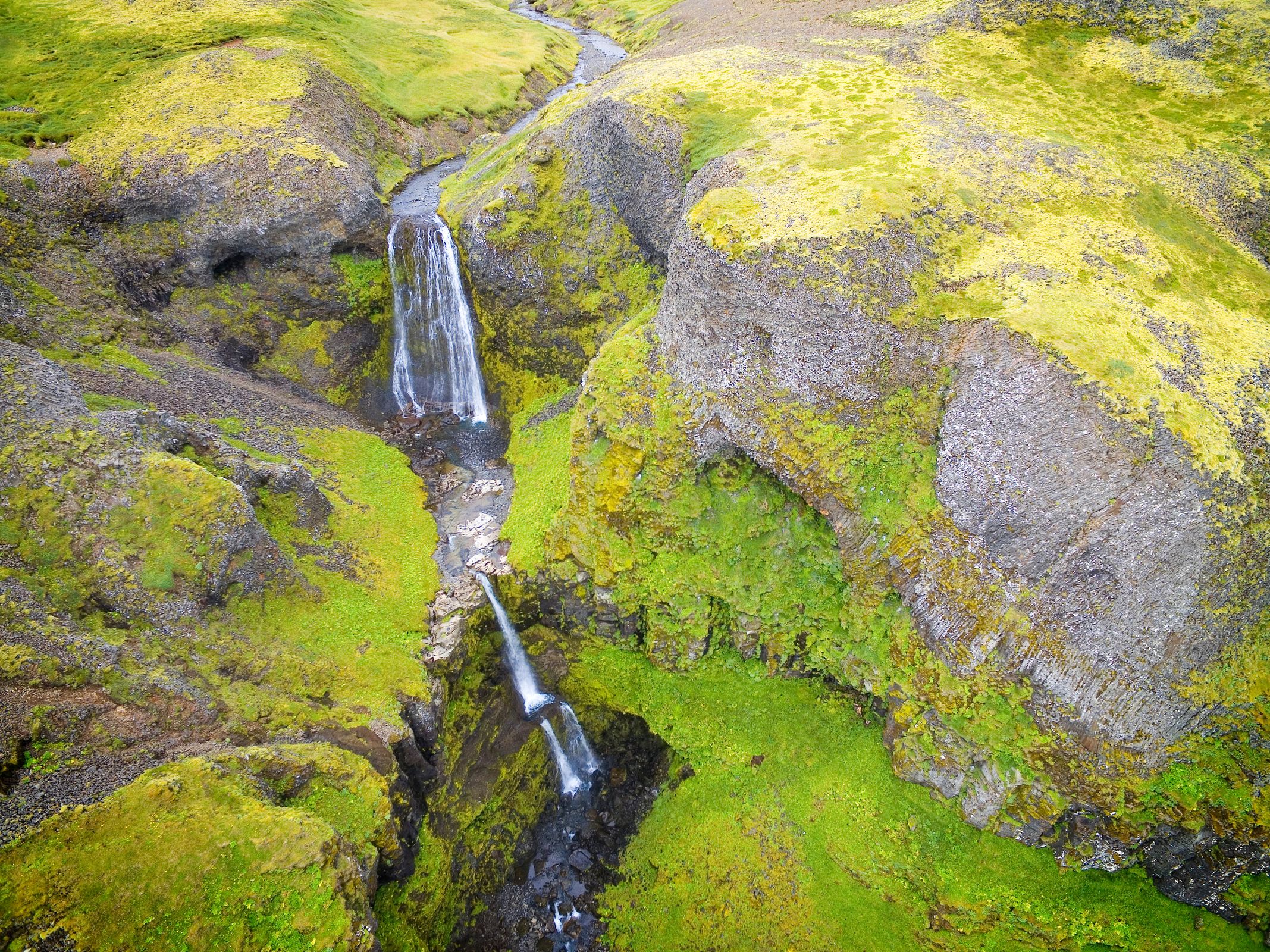 Aerial view of a waterfall flowing through a lush, mossy green canyon.