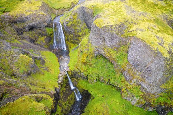 Aerial view of a waterfall flowing through a lush, mossy green canyon.