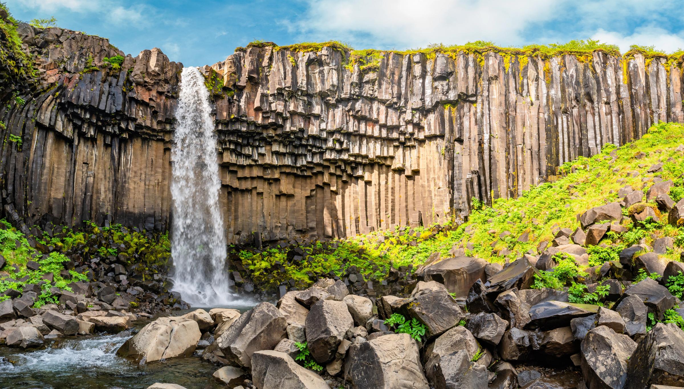 a waterfall falling from a cliff with basalt columns on its wall