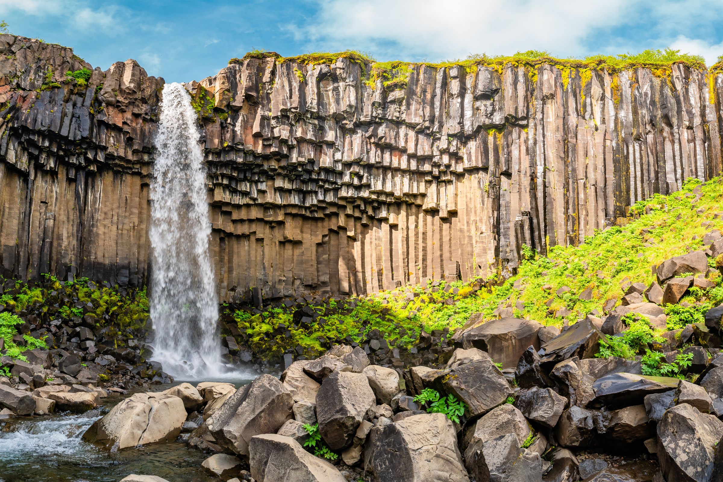 a waterfall falling from a cliff with basalt columns on its wall