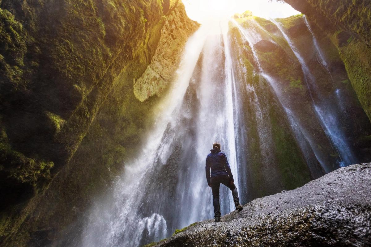 a man is standing on a rock in front of a waterfall .