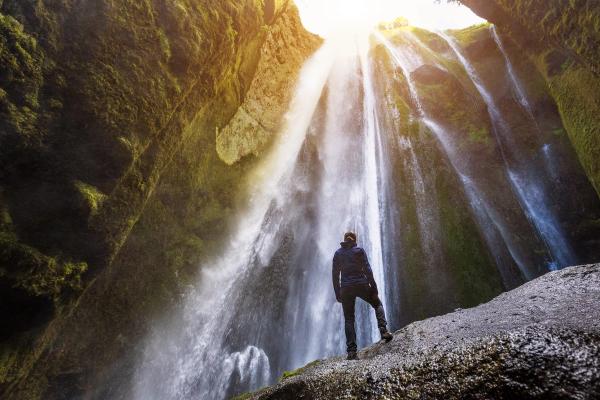 a man is standing on a rock in front of a waterfall .
