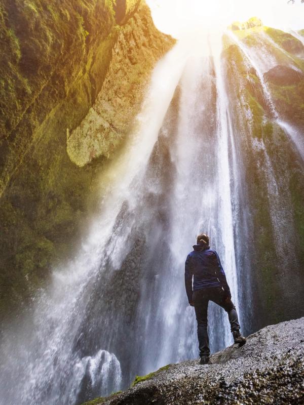 a man is standing on a rock in front of a waterfall .