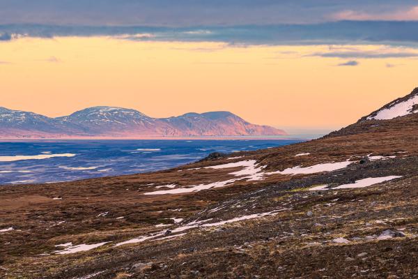 a sunset over a mountain range with mountains in the background and a body of water in the foreground .