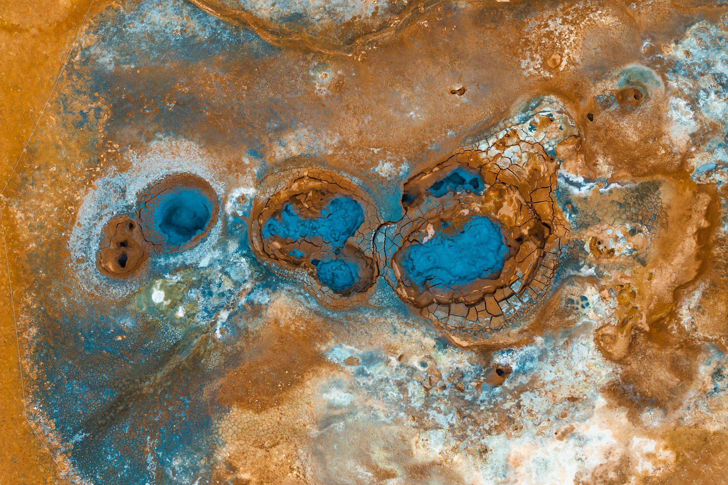 Vista aérea de brillantes pozas azul turquesa sobre una tierra agrietada de tonos naranjas y marrones.
