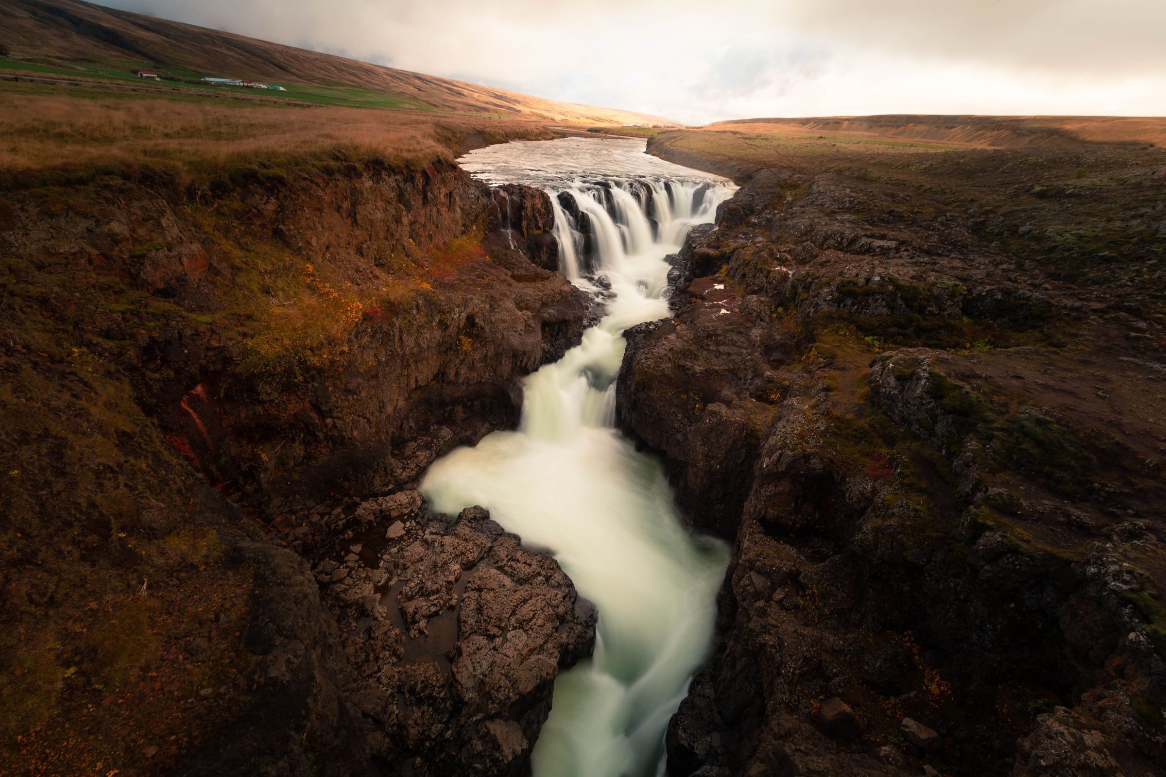 A powerful waterfall cascades through a dark, rocky canyon, with blurred white water.