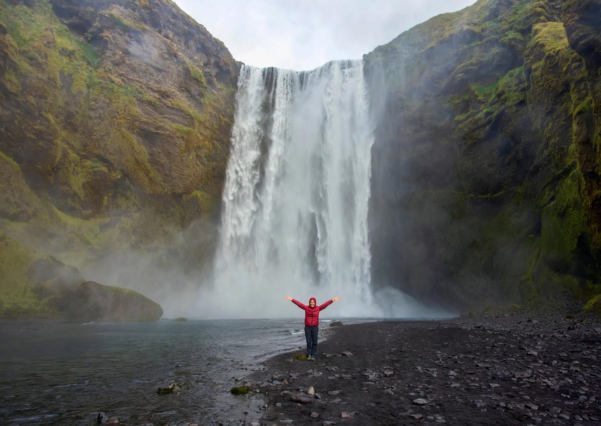 Mujer en frente de Skógafoss levantando los brazos