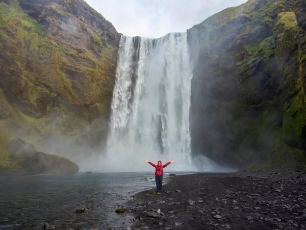 Mujer en frente de Skógafoss levantando los brazos