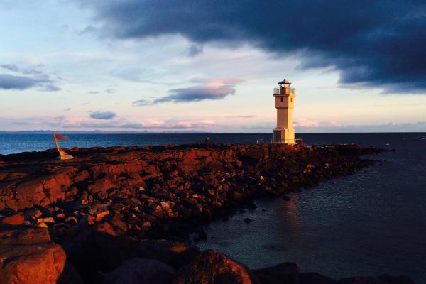 un delgado faro blanco junto al mar con la luz cálida del atardecer