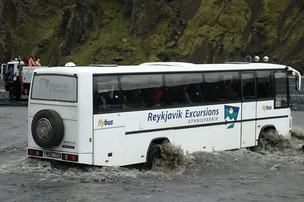 a white bus from reykjavik excursions is driving through a river