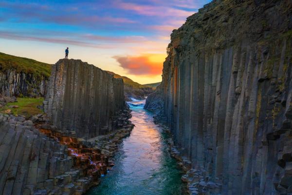 Person on a basalt column overlooking a river canyon at sunset.