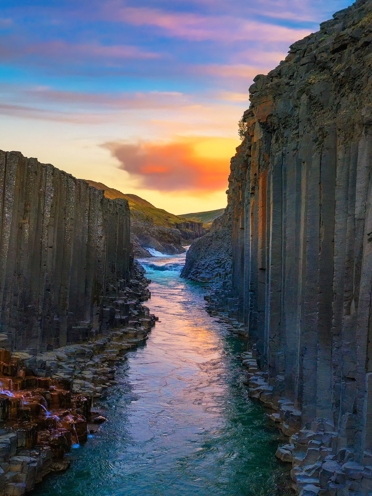 Person on a basalt column overlooking a river canyon at sunset.