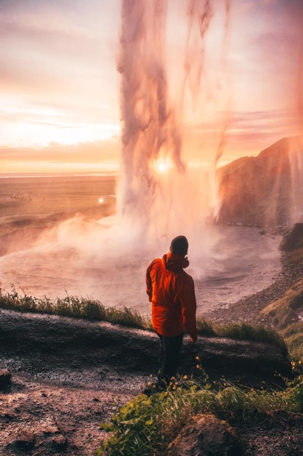 Hombre con un abrigo naranja detrás de una cascada