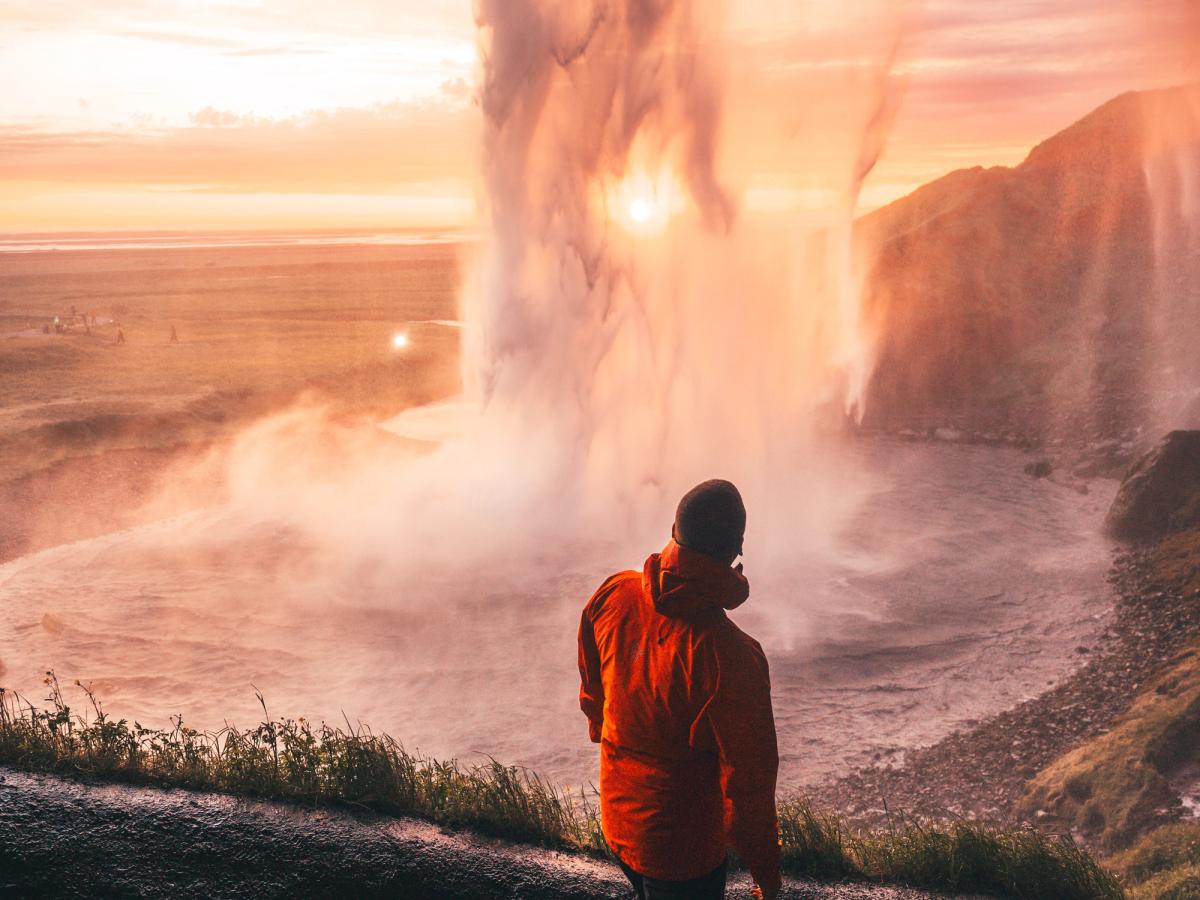 Hombre con un abrigo naranja detrás de una cascada