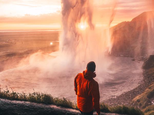 a man in an orange jacket stands in front of a waterfall